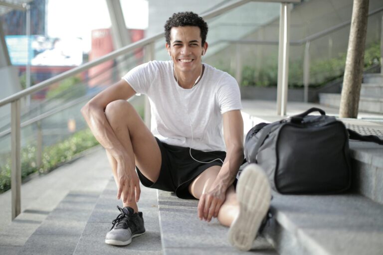 Happy young African American male athlete listening to music and resting after training on stairs on street