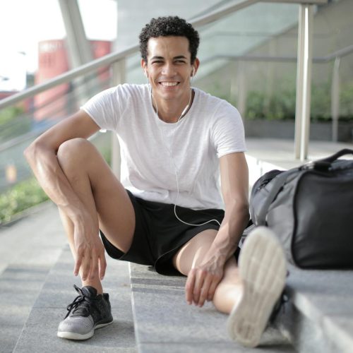 Happy young African American male athlete listening to music and resting after training on stairs on street